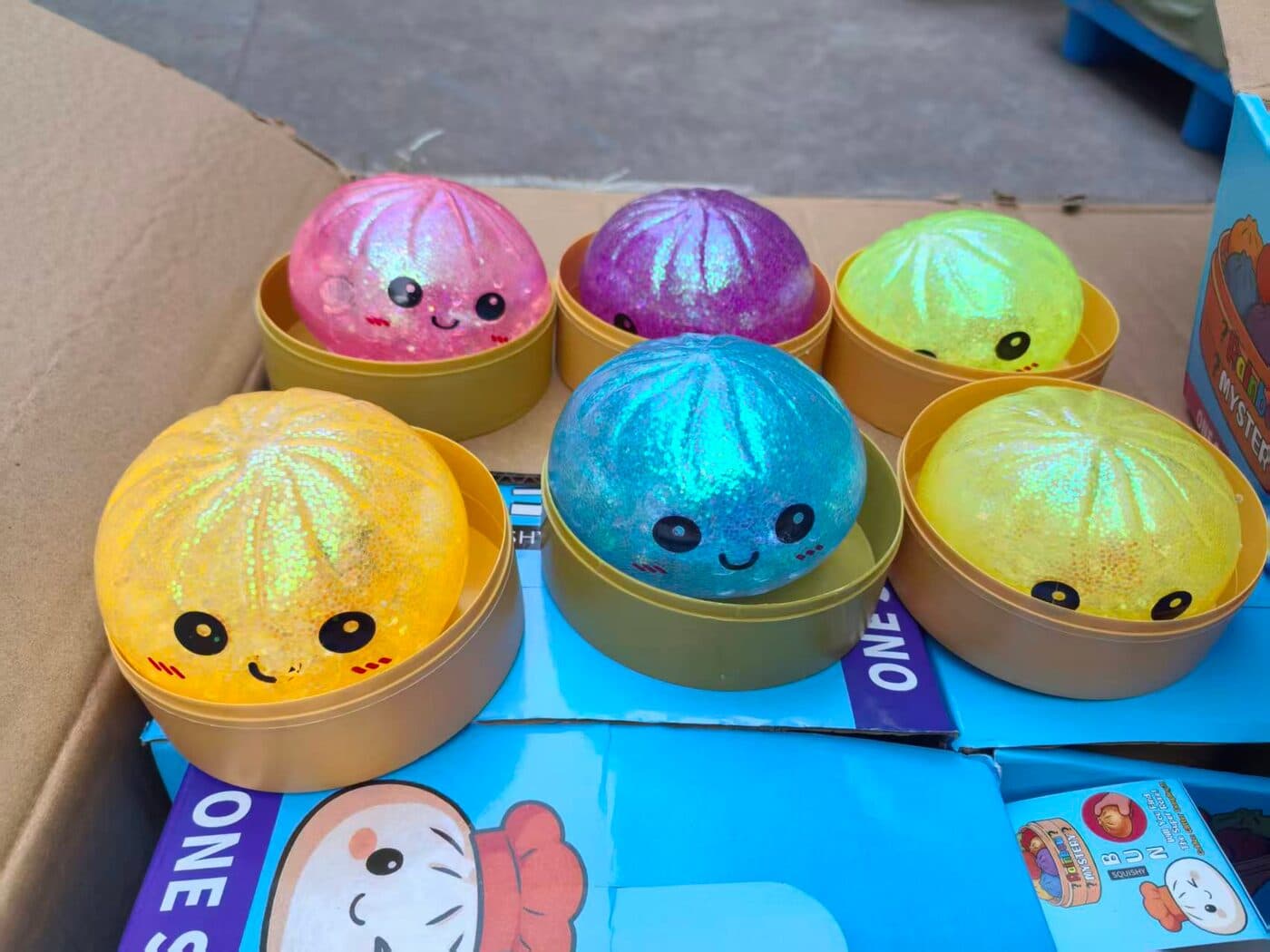 Seis squishies de dumpling con escarcha tornasol en rosa, morado, verde limón, amarillo y azul turquesa, en sus vaporeras